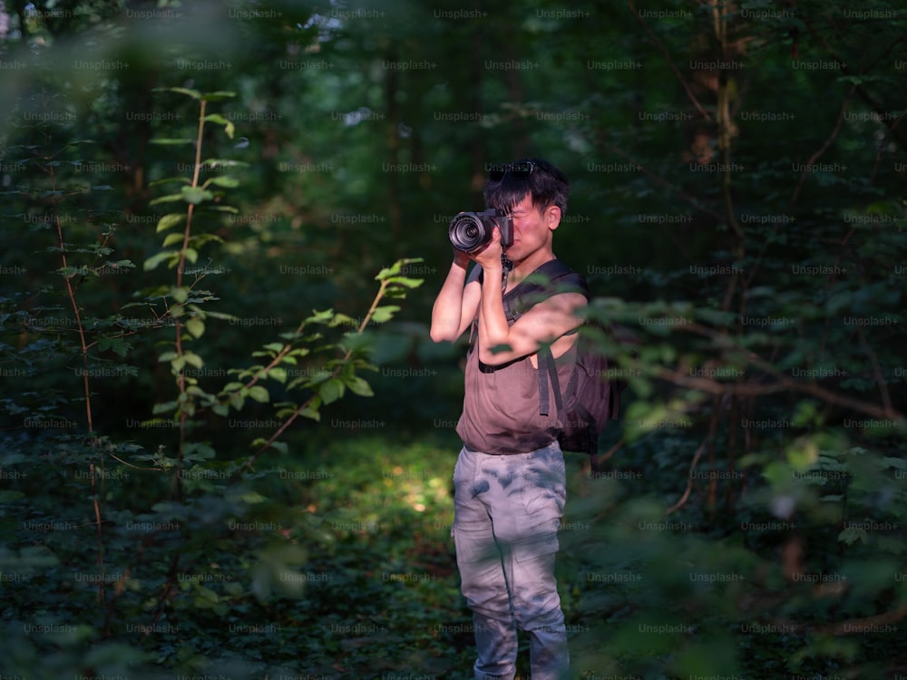 um homem parado na floresta tirando uma foto com uma câmera