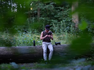 Un hombre sentado en un tronco mirando su teléfono celular