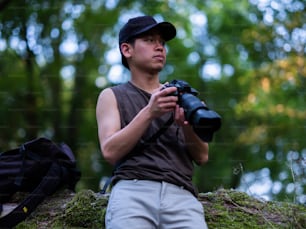 Un hombre sosteniendo una cámara mientras está sentado en una roca cubierta de musgo