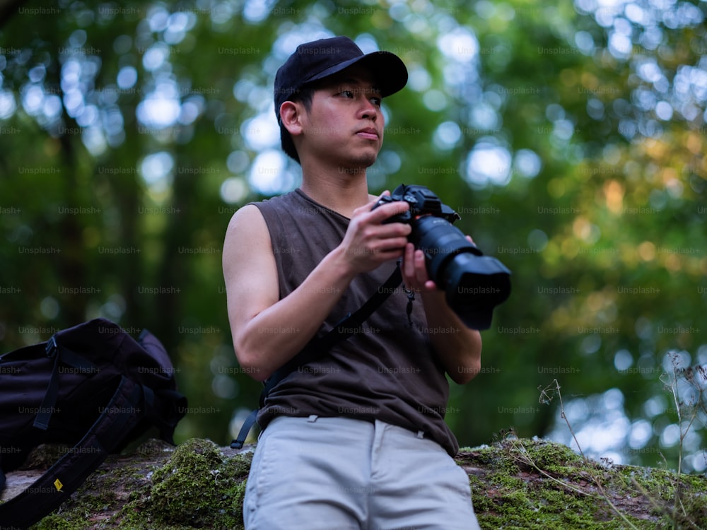 a man holding a camera while sitting on a moss covered rock