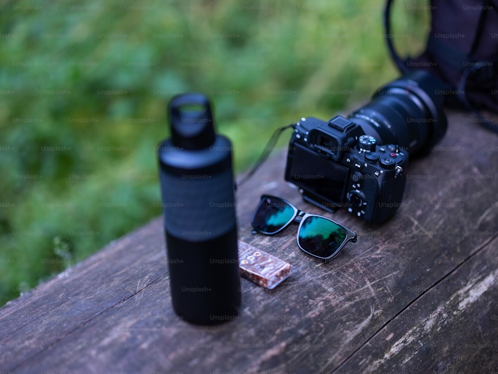 uma máquina fotográfica, óculos escuros e uma garrafa de água sentada num banco