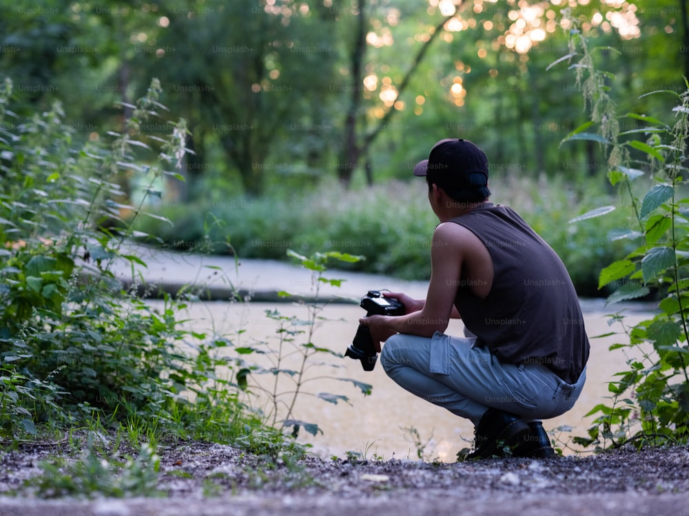 Un uomo inginocchiato vicino a un fiume con in mano una macchina fotografica