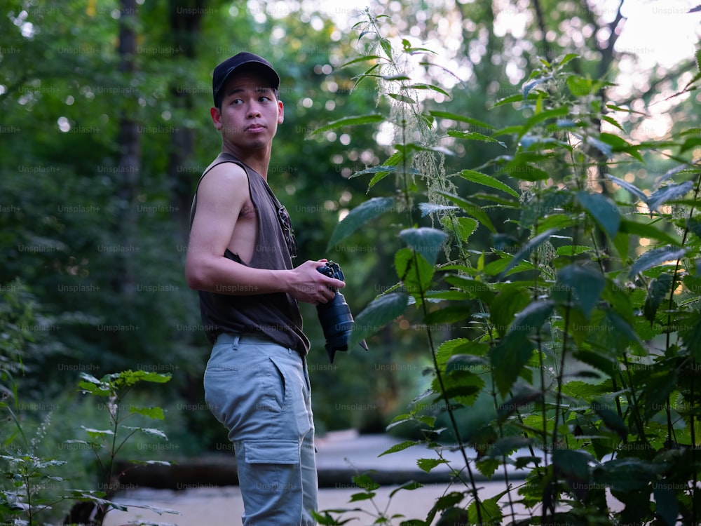 um homem parado na floresta segurando uma câmera