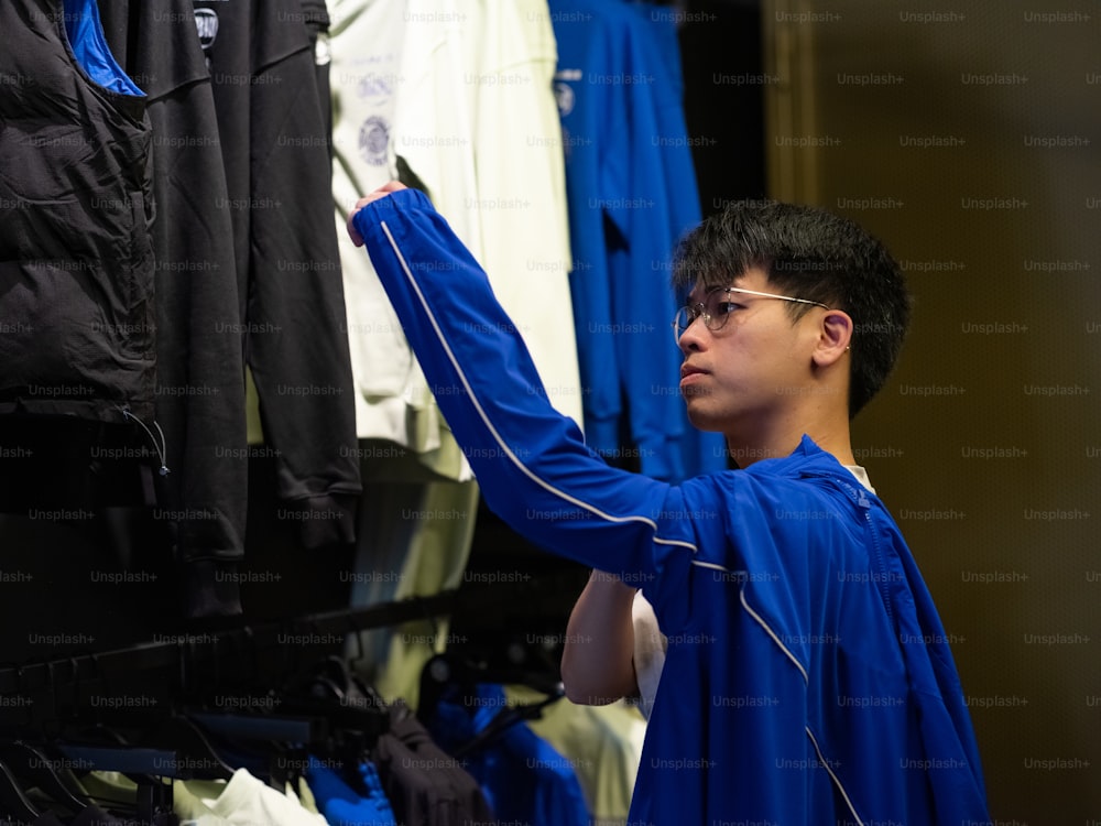 a boy in a blue shirt is looking at a rack of shirts