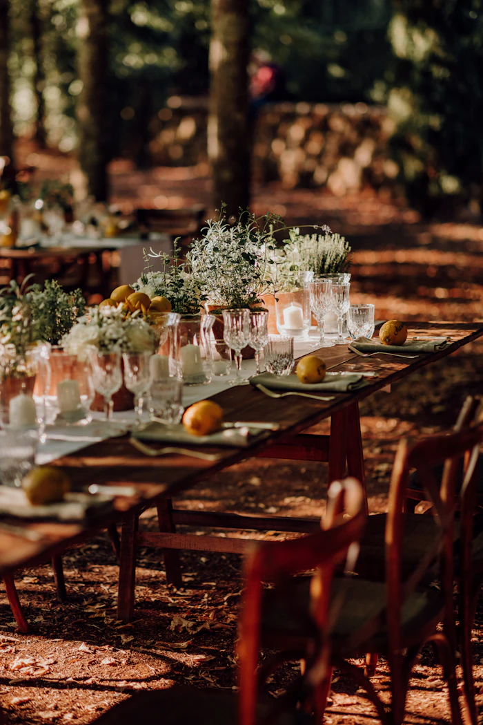 A long reception table set with flowers and glassware in the woods