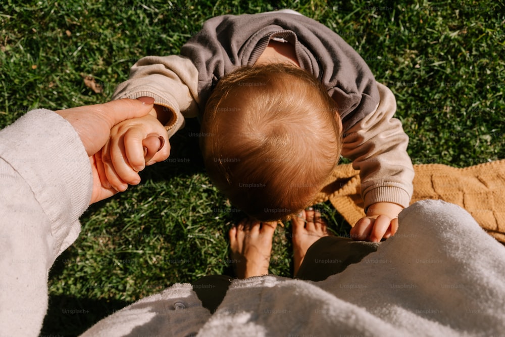 a person holding a baby's hand while laying on the ground