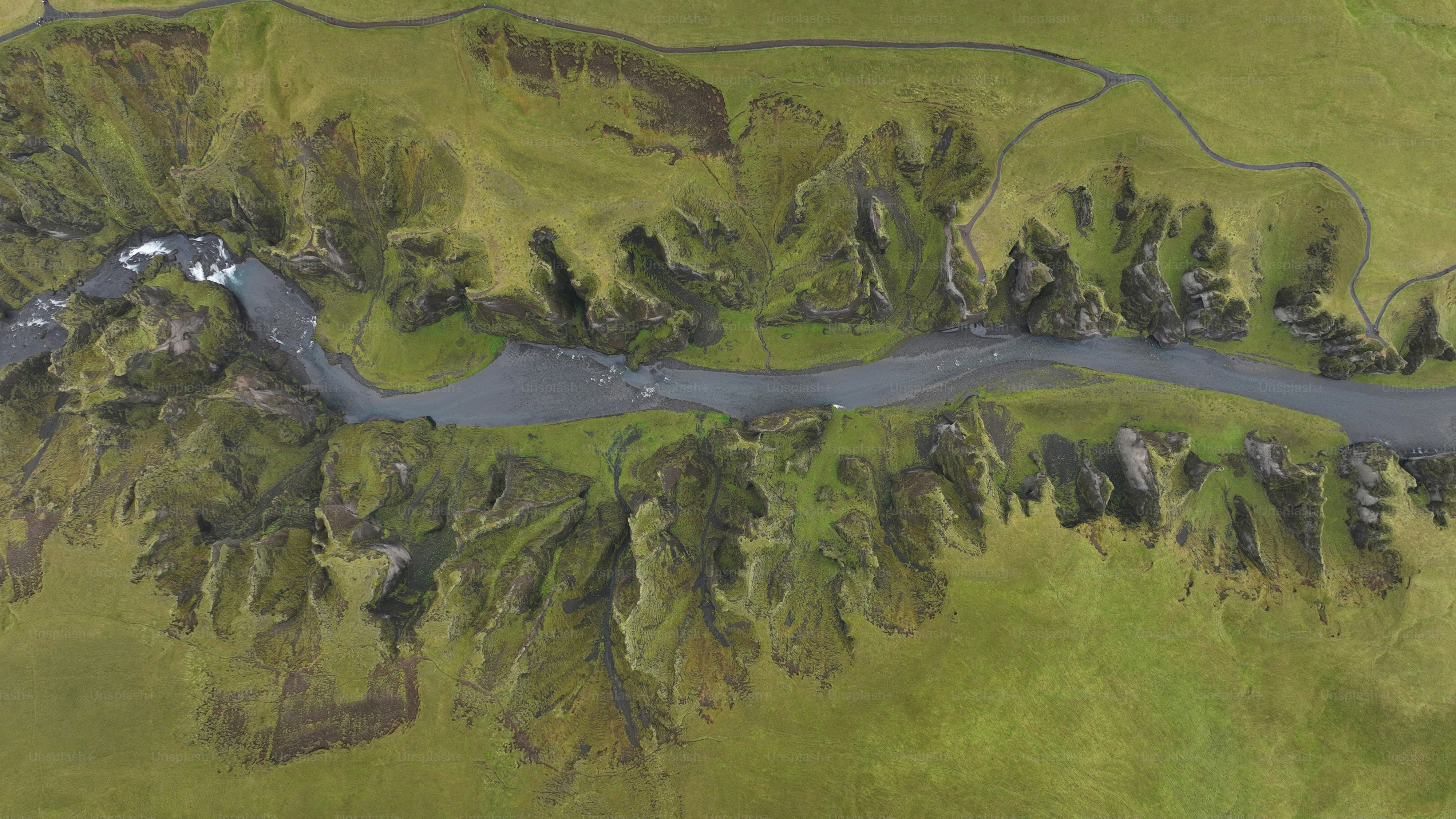 an aerial view of a river running through a lush green field