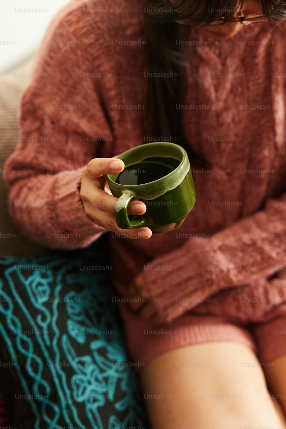 a woman sitting on a couch holding a green cup