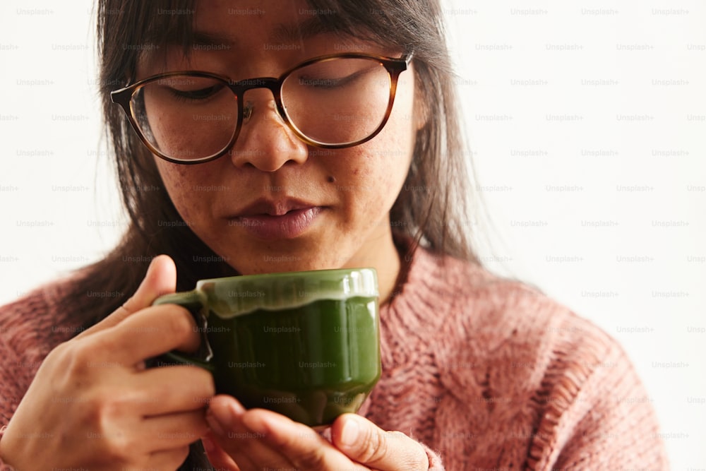 Una mujer con gafas sosteniendo una taza verde