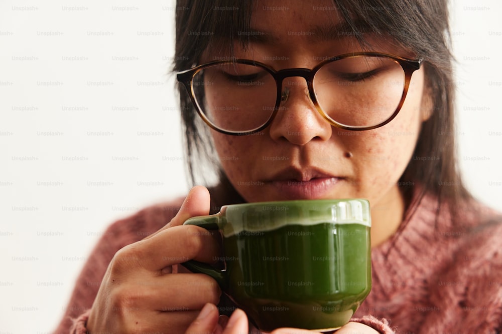 Una mujer con gafas sosteniendo una taza verde