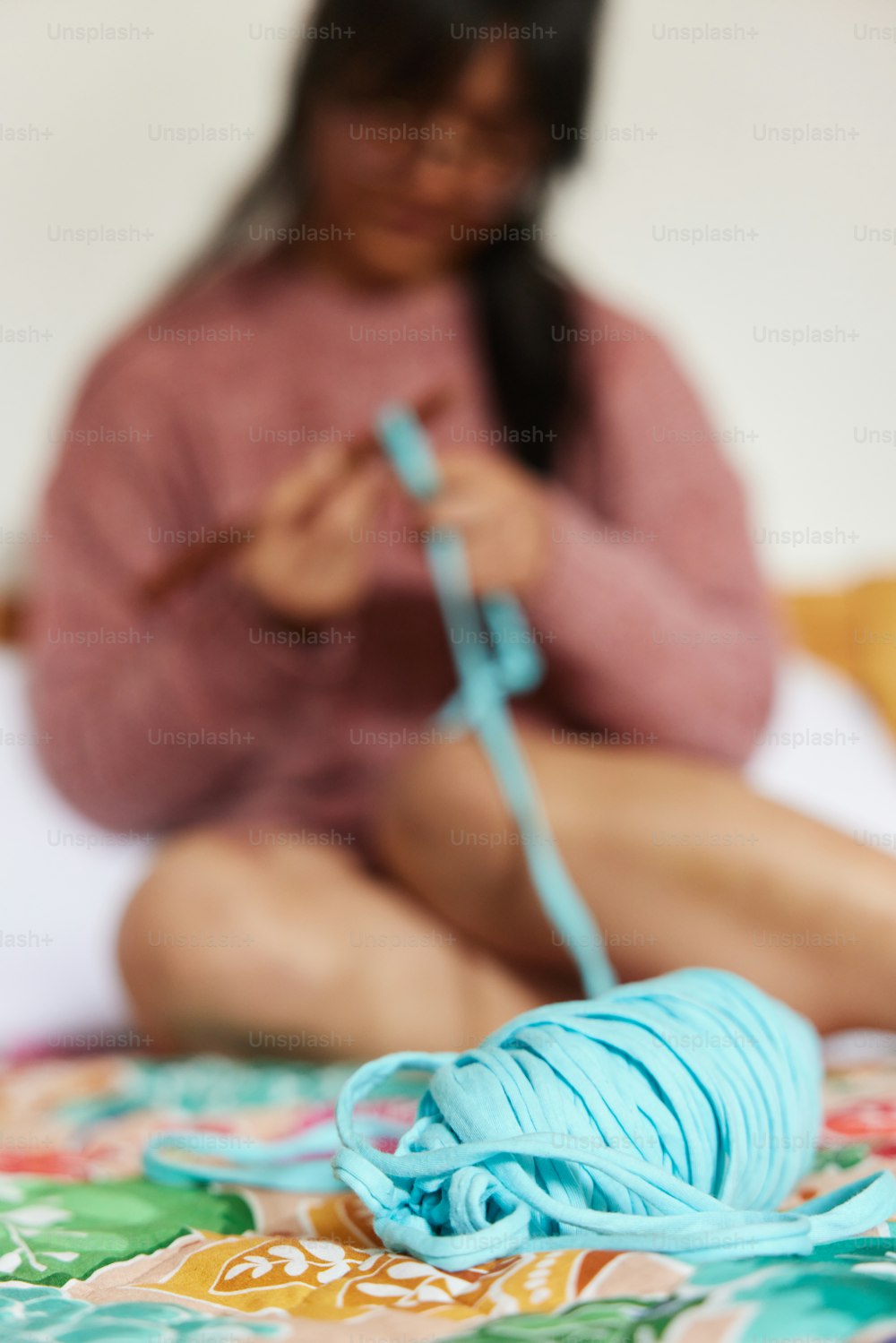 a woman sitting on a bed knitting a ball of yarn