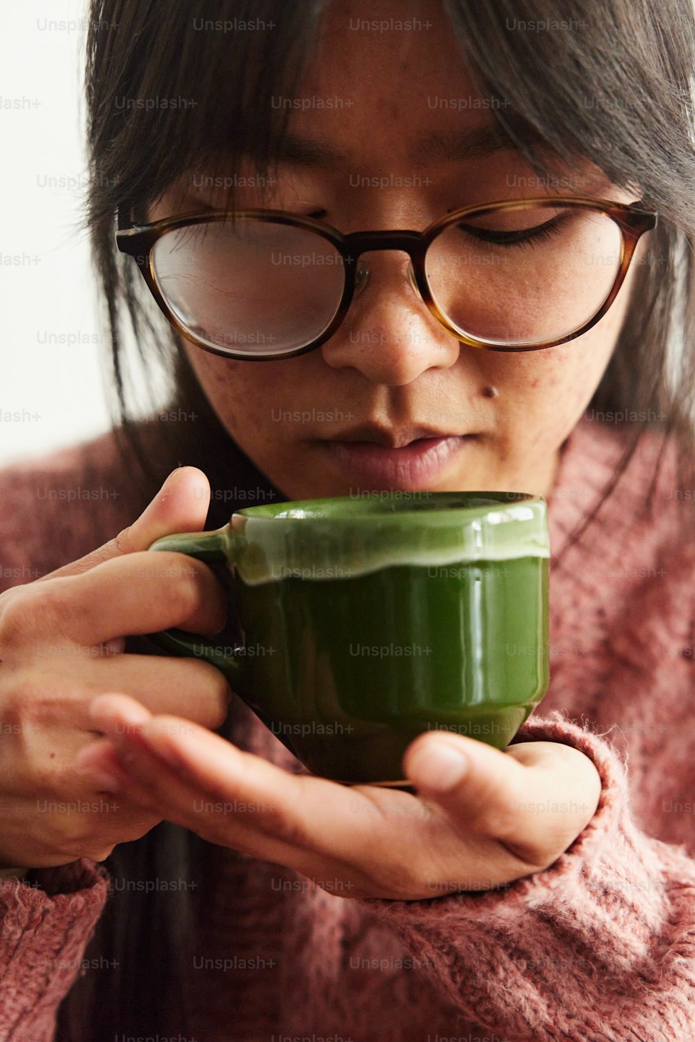 Eine Frau mit Brille, die eine grüne Tasse hält