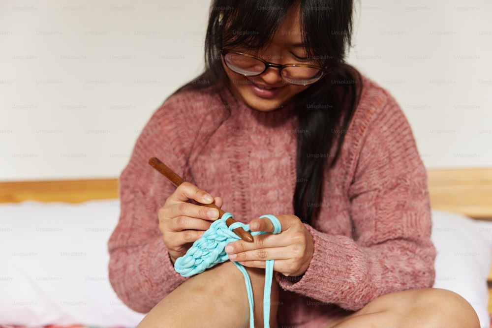 a woman sitting on a bed holding a crochet hook