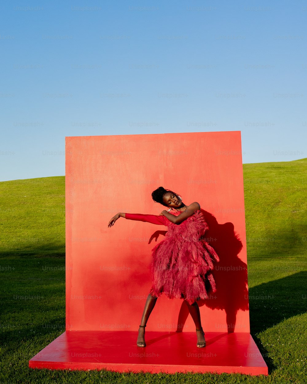 분홍색 드레스를 입은 여자가 빨간 조각상 앞에 서 있다