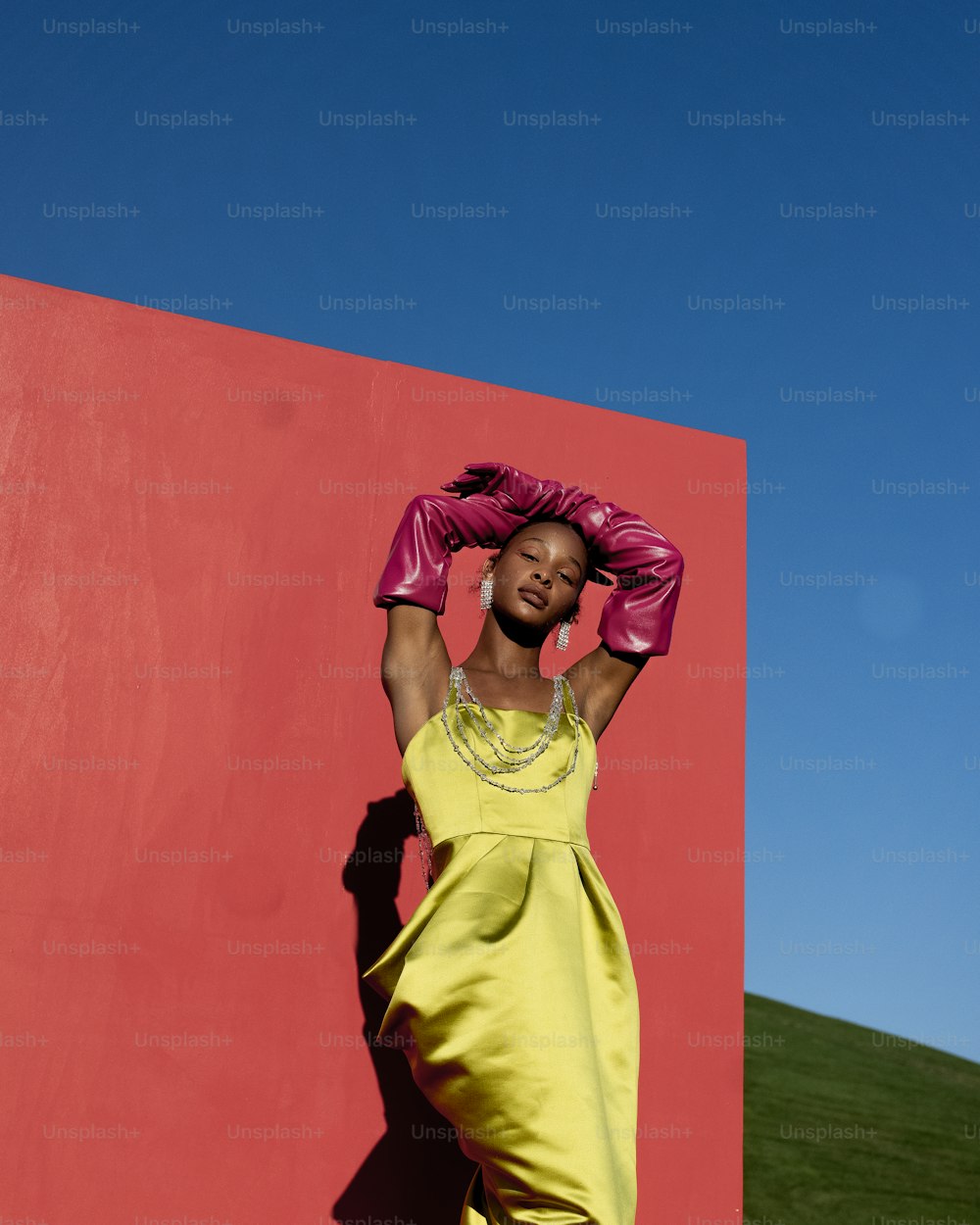 a woman in a yellow dress leaning against a pink wall