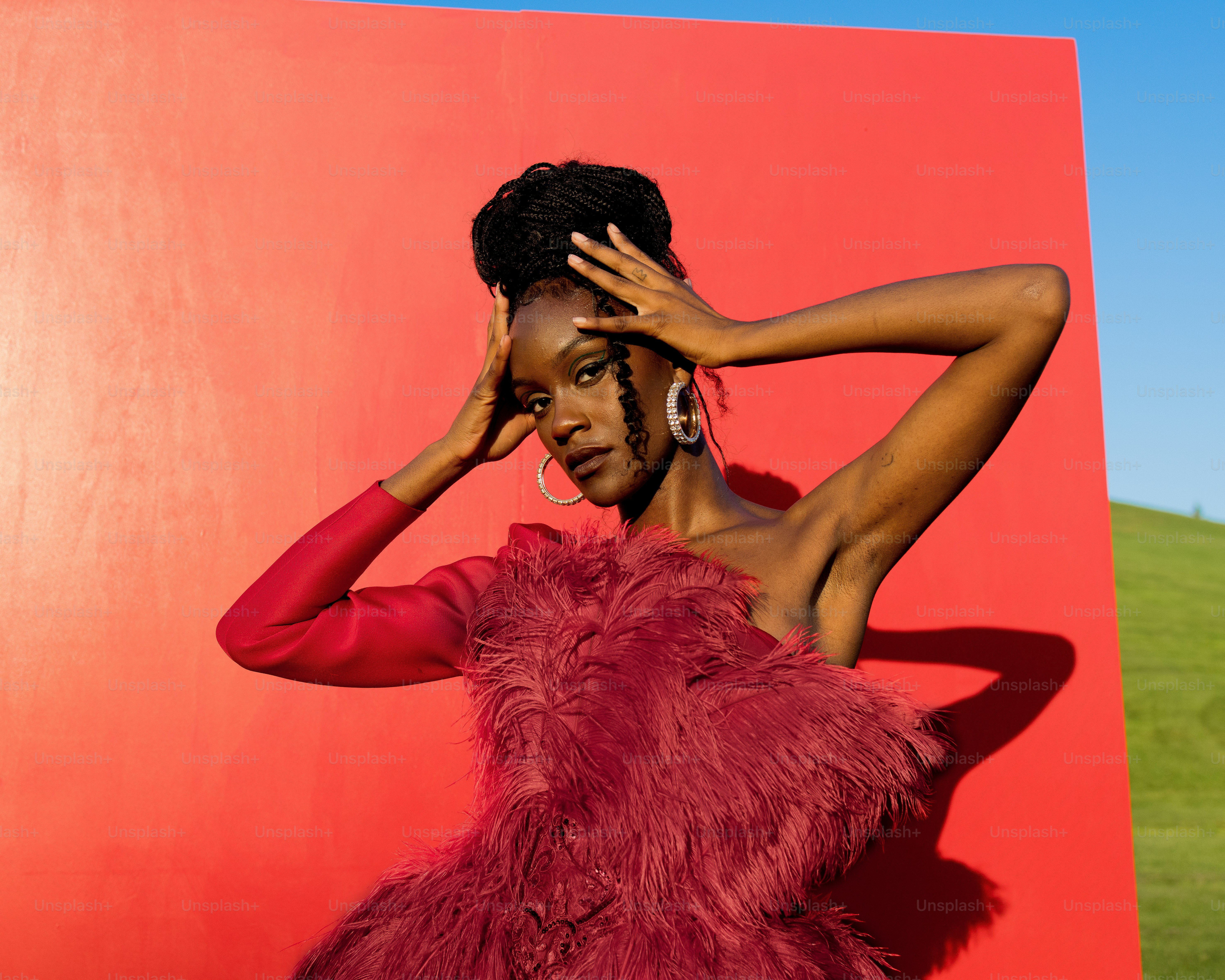 a woman in a red feathered dress poses in front of a red wall