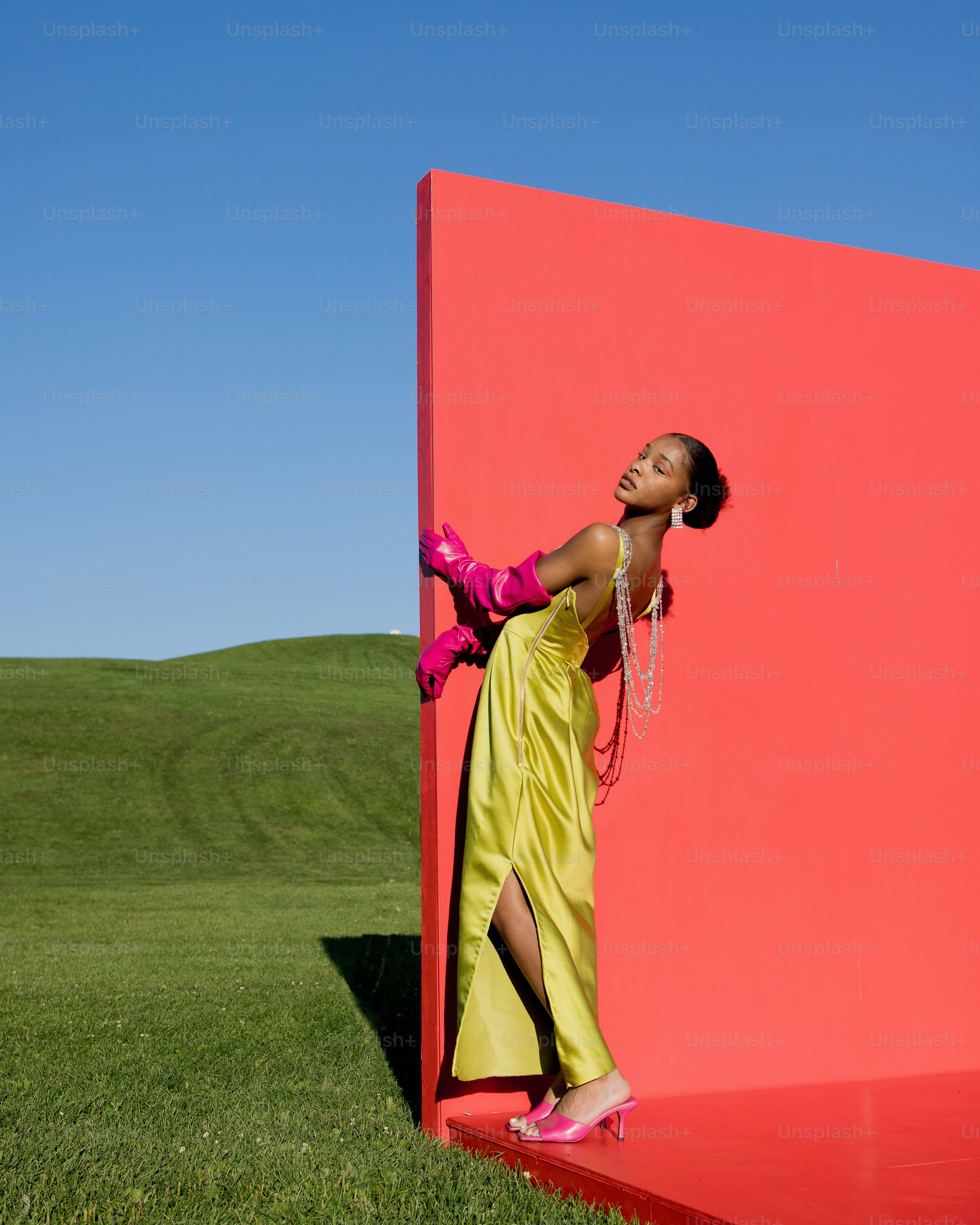 a woman in a yellow dress leaning against a red wall