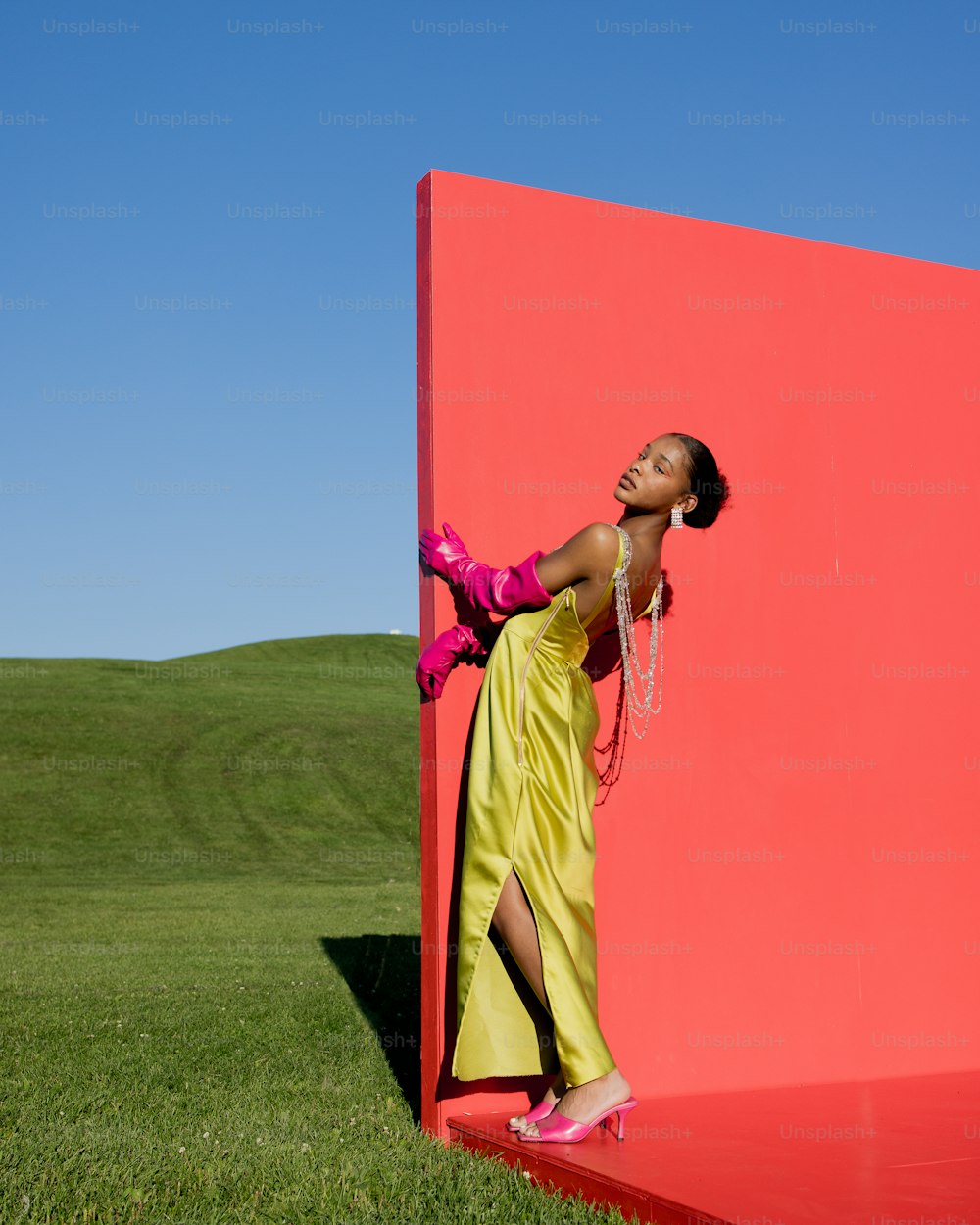 Una donna in un vestito giallo appoggiata a un muro rosso