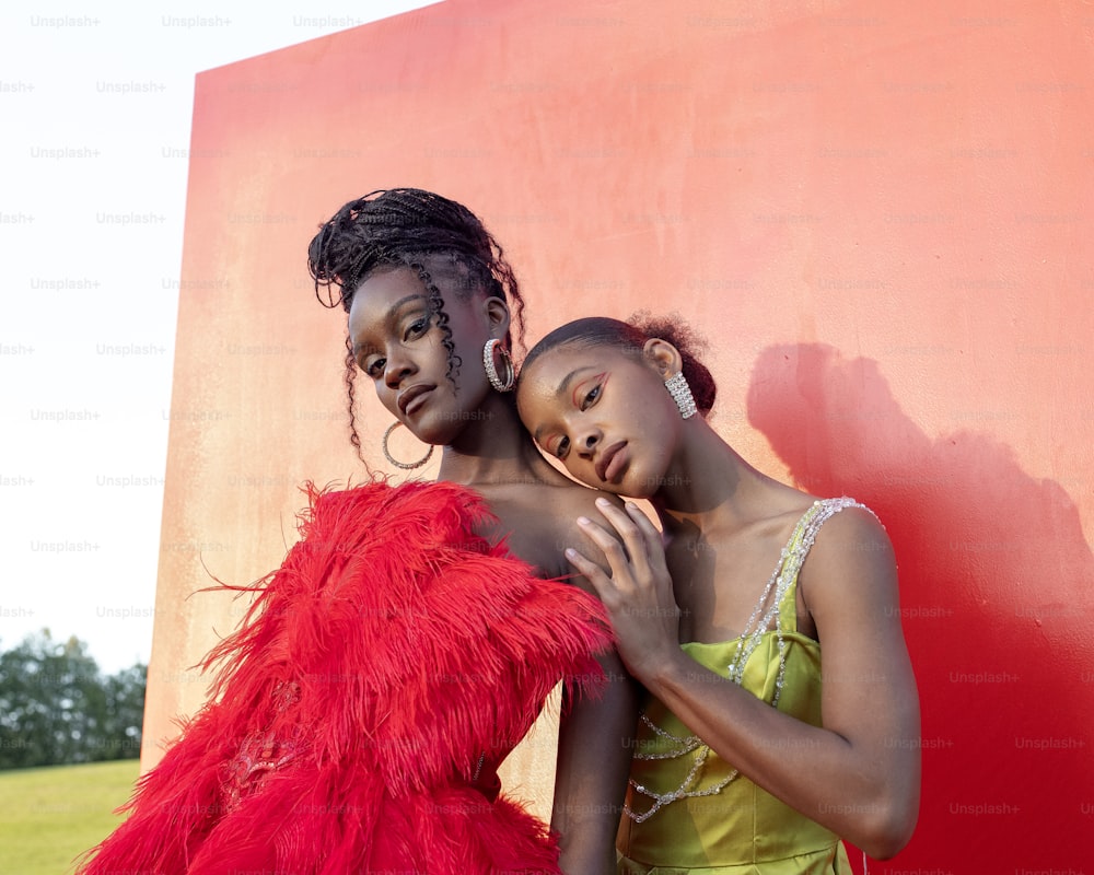 two women standing next to each other in front of a red wall