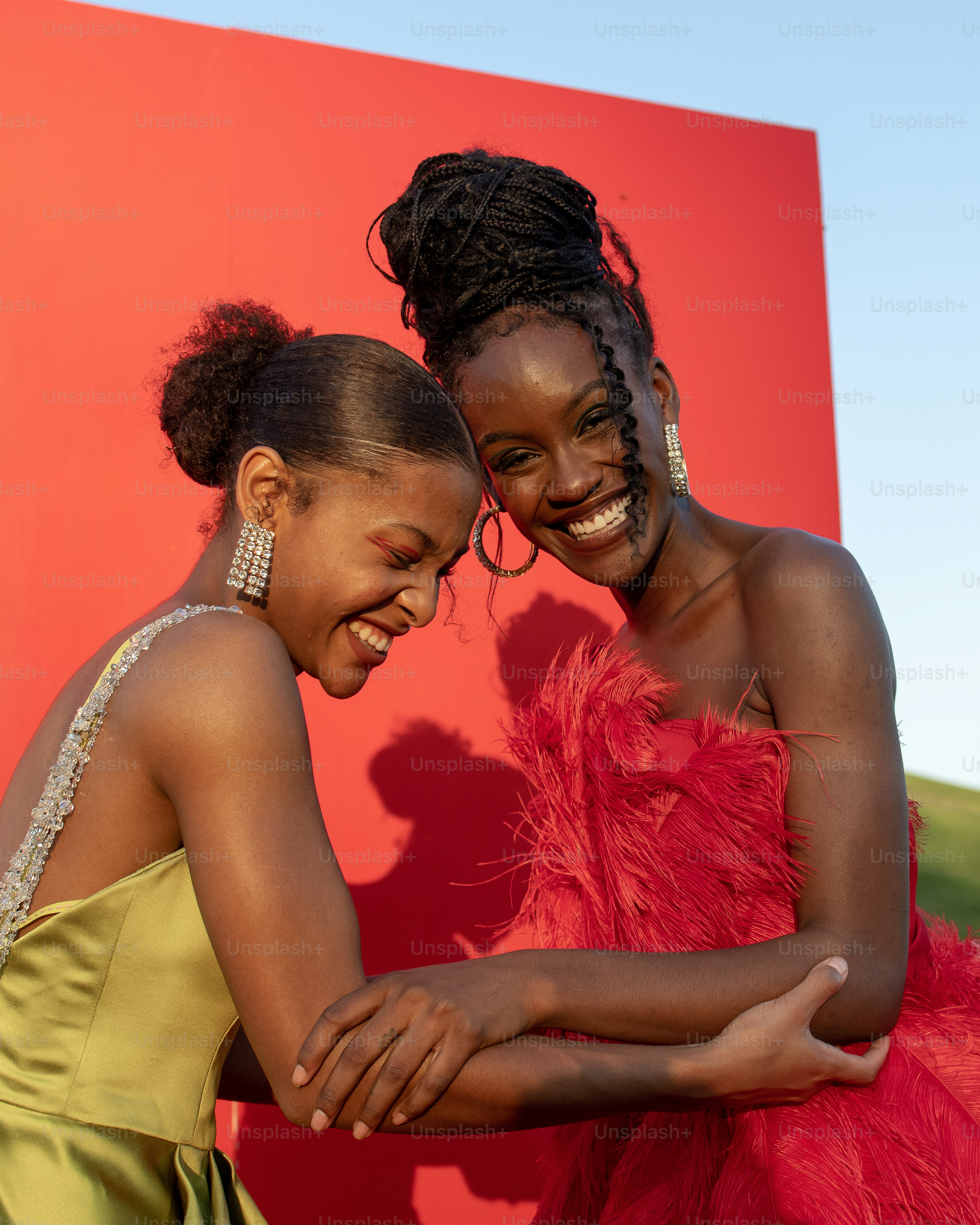two women are hugging each other in front of a red wall
