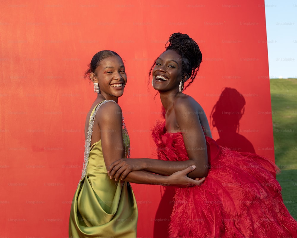 two women standing next to each other in front of a red wall