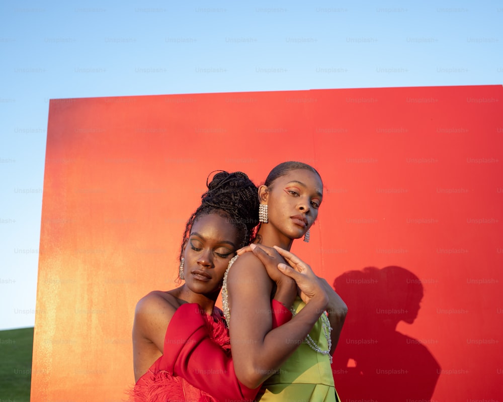two women standing next to each other in front of a red wall