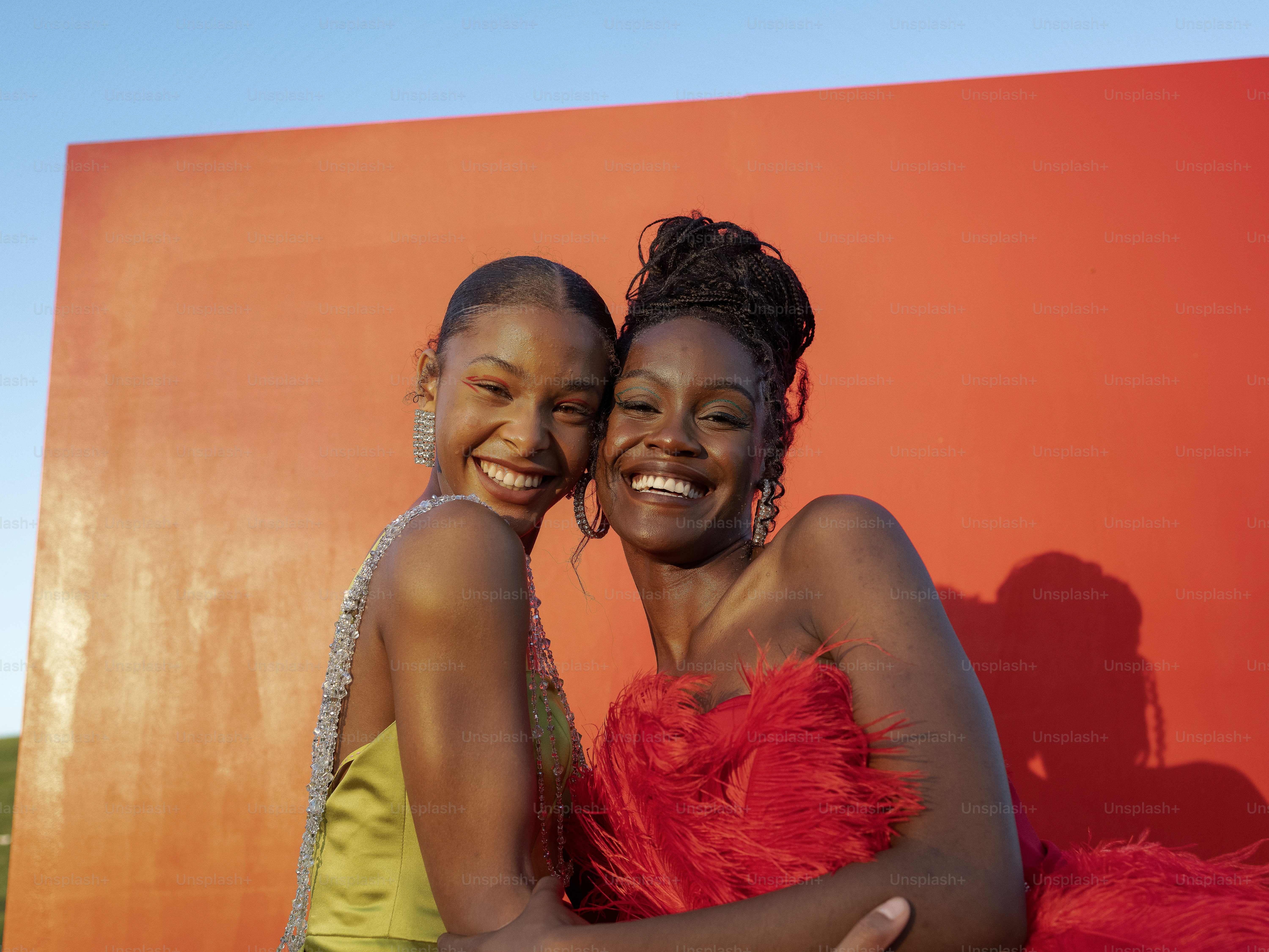 two young women hugging each other in front of a red wall