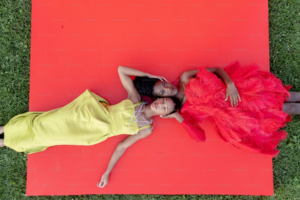Zwei Mädchen liegen auf einer roten Matte im Gras