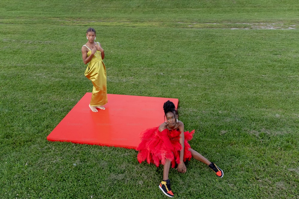two girls sitting on a red mat in the grass