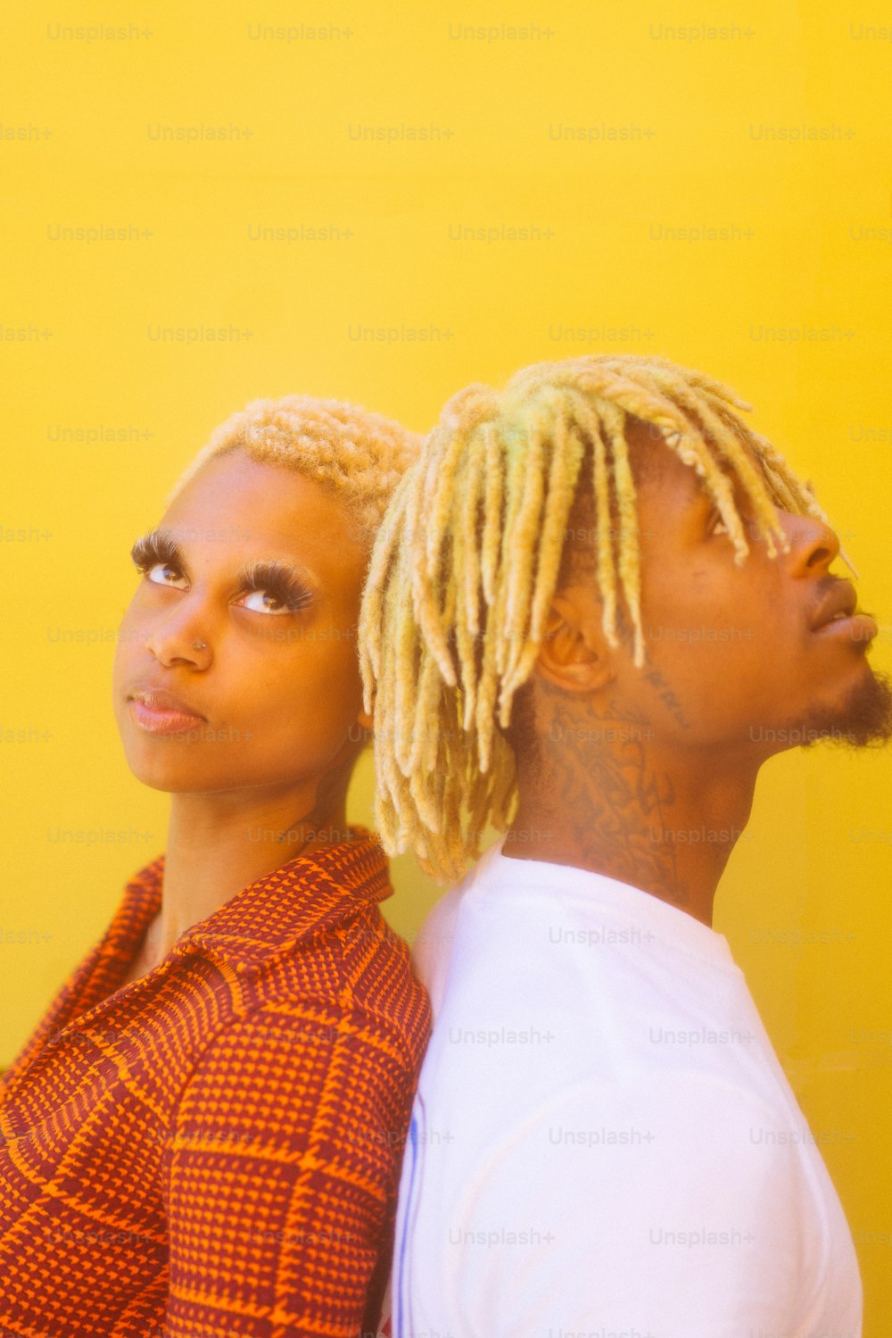 a man and a woman with dreadlocks standing in front of a yellow wall
