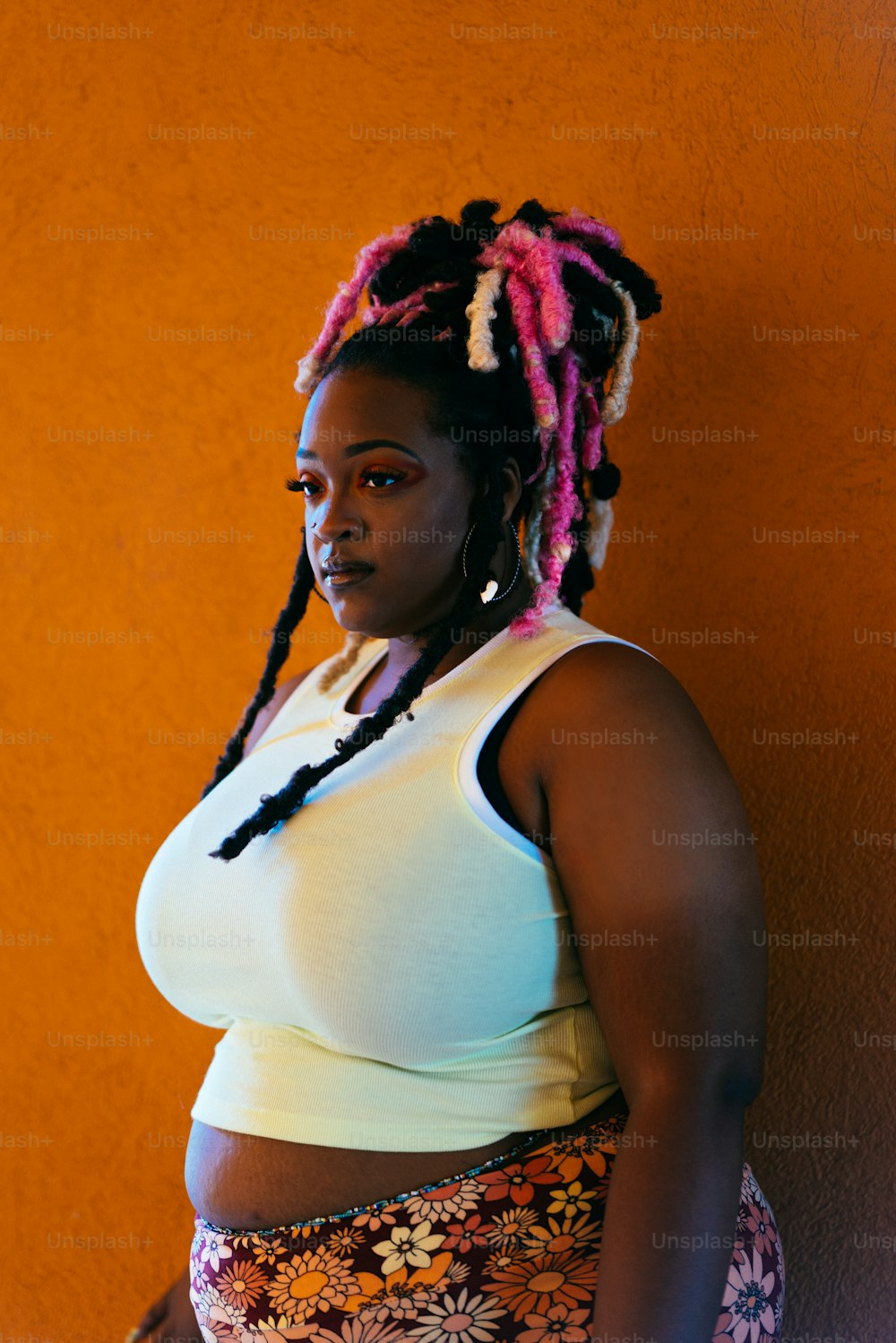 a woman with pink dreadlocks standing against a wall