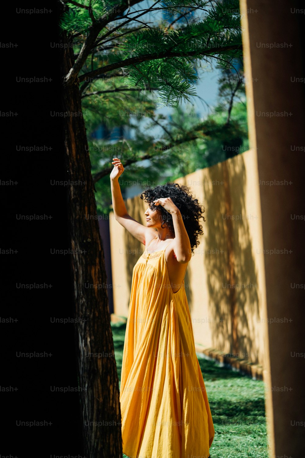 木の隣に立つ黄色いドレスを着た女性
