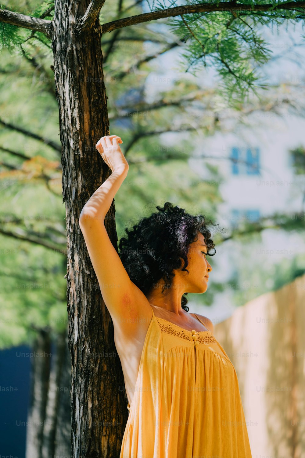 a woman in a yellow dress standing next to a tree