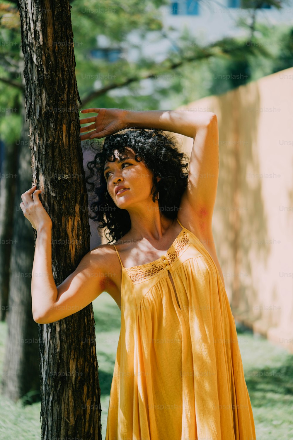 a woman in a yellow dress leaning against a tree