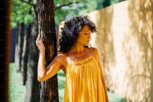a woman in a yellow dress leaning against a tree