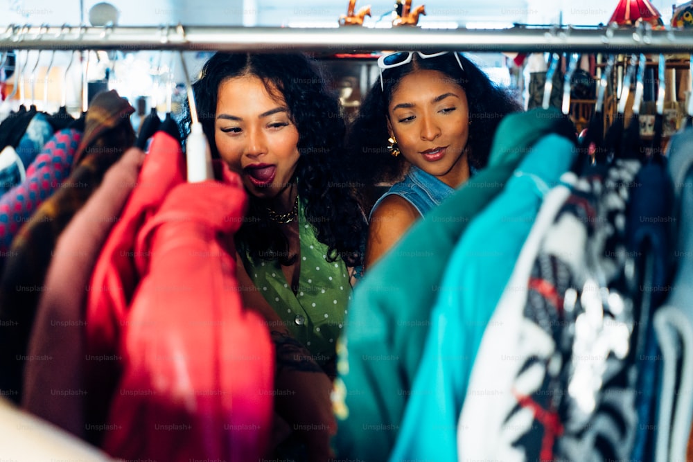 a couple of women standing next to each other in front of a rack of shirts
