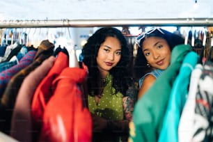 two women standing next to each other in front of a rack of clothes