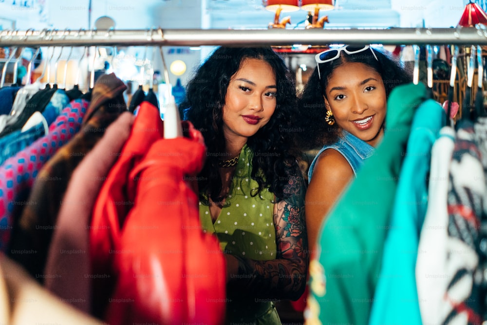 two women standing next to each other in front of a rack of clothes