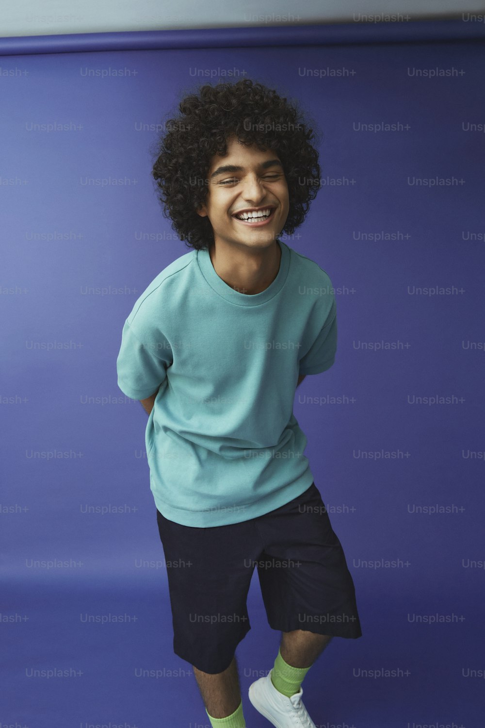 a young man with curly hair wearing a blue shirt and black shorts