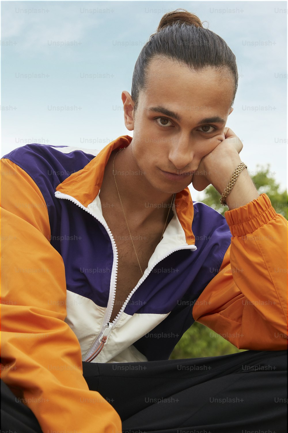 a woman sitting on the ground wearing an orange and purple jacket