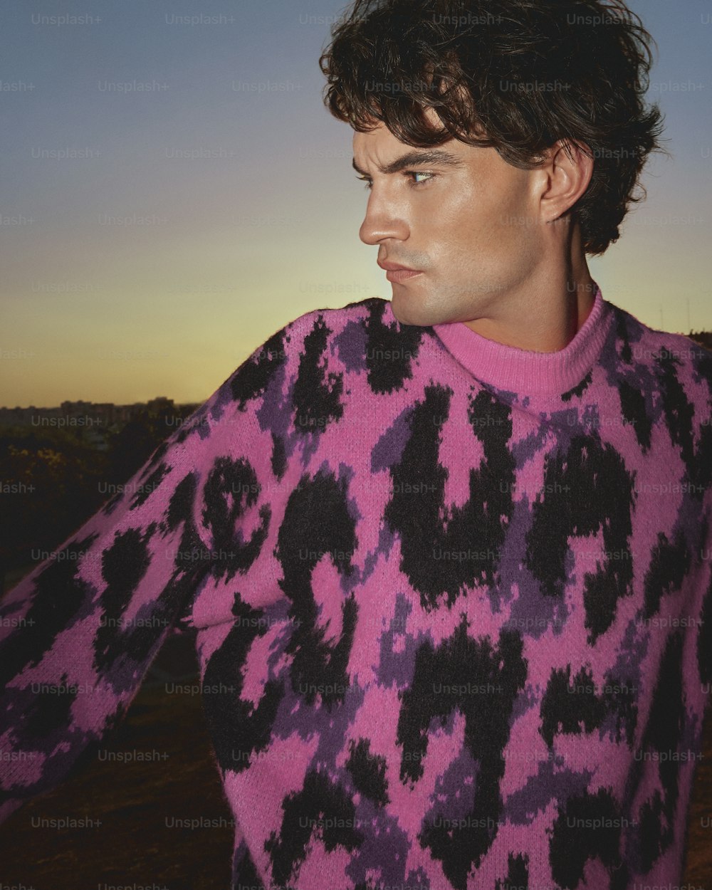 a man in a pink and black sweater looks off into the distance