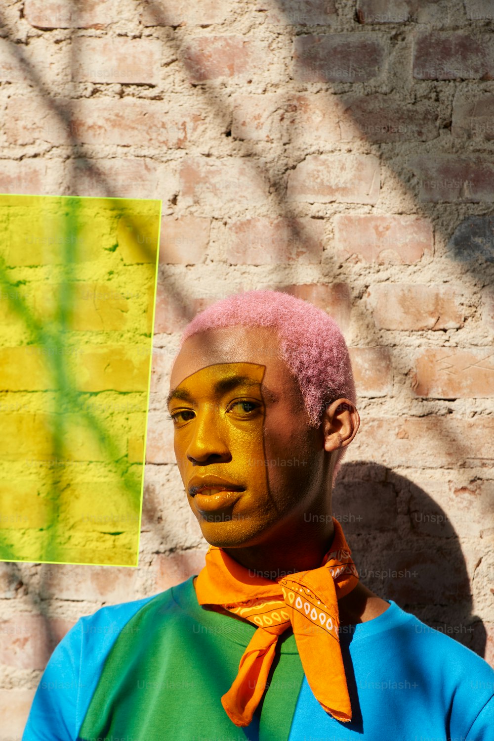 a man with pink hair standing in front of a brick wall