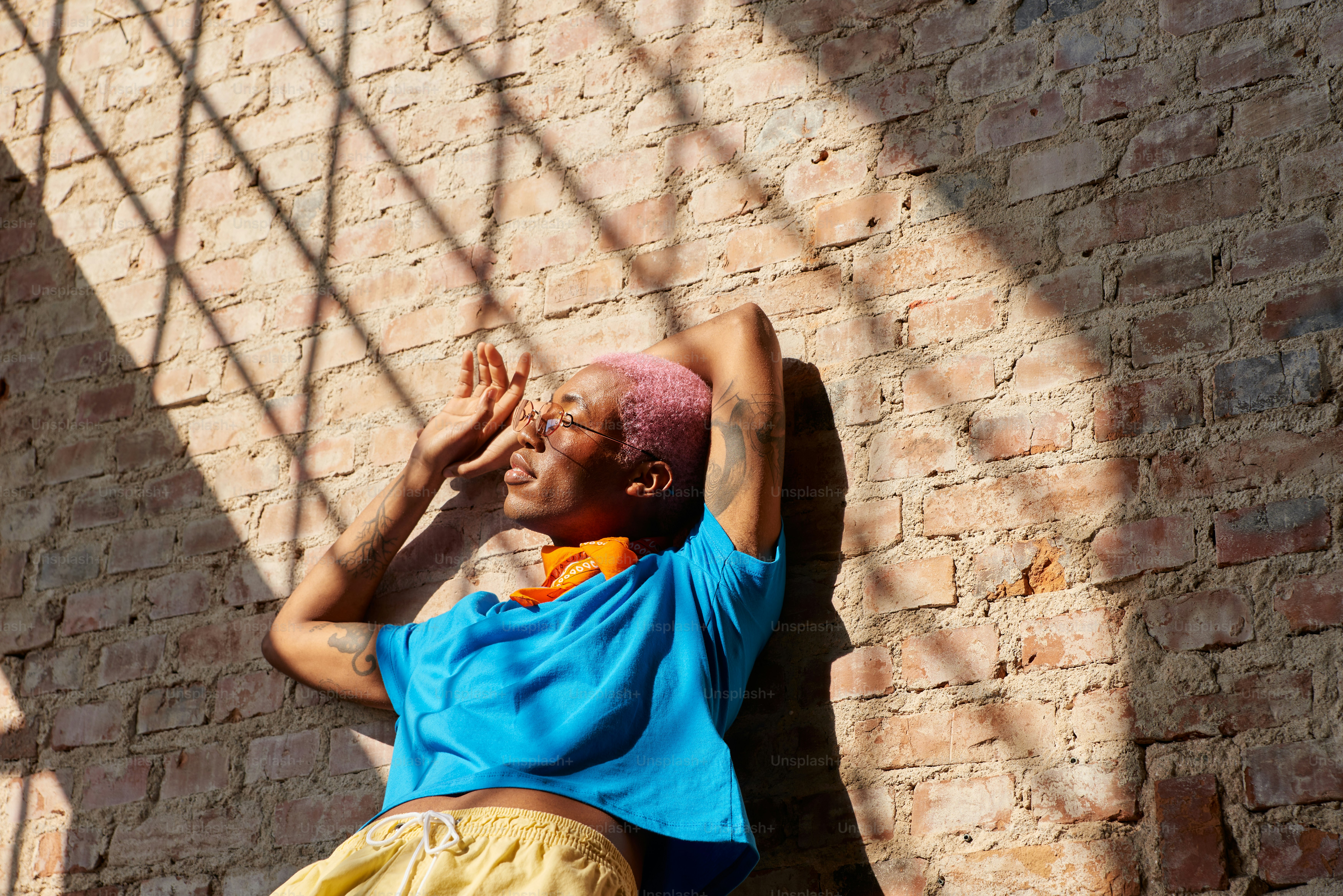 Un uomo appoggiato a un muro di mattoni con le mani sulla testa