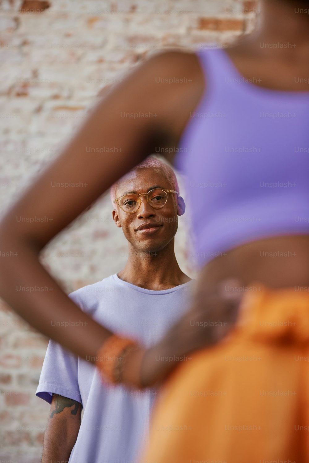 a man with glasses standing in front of a brick wall