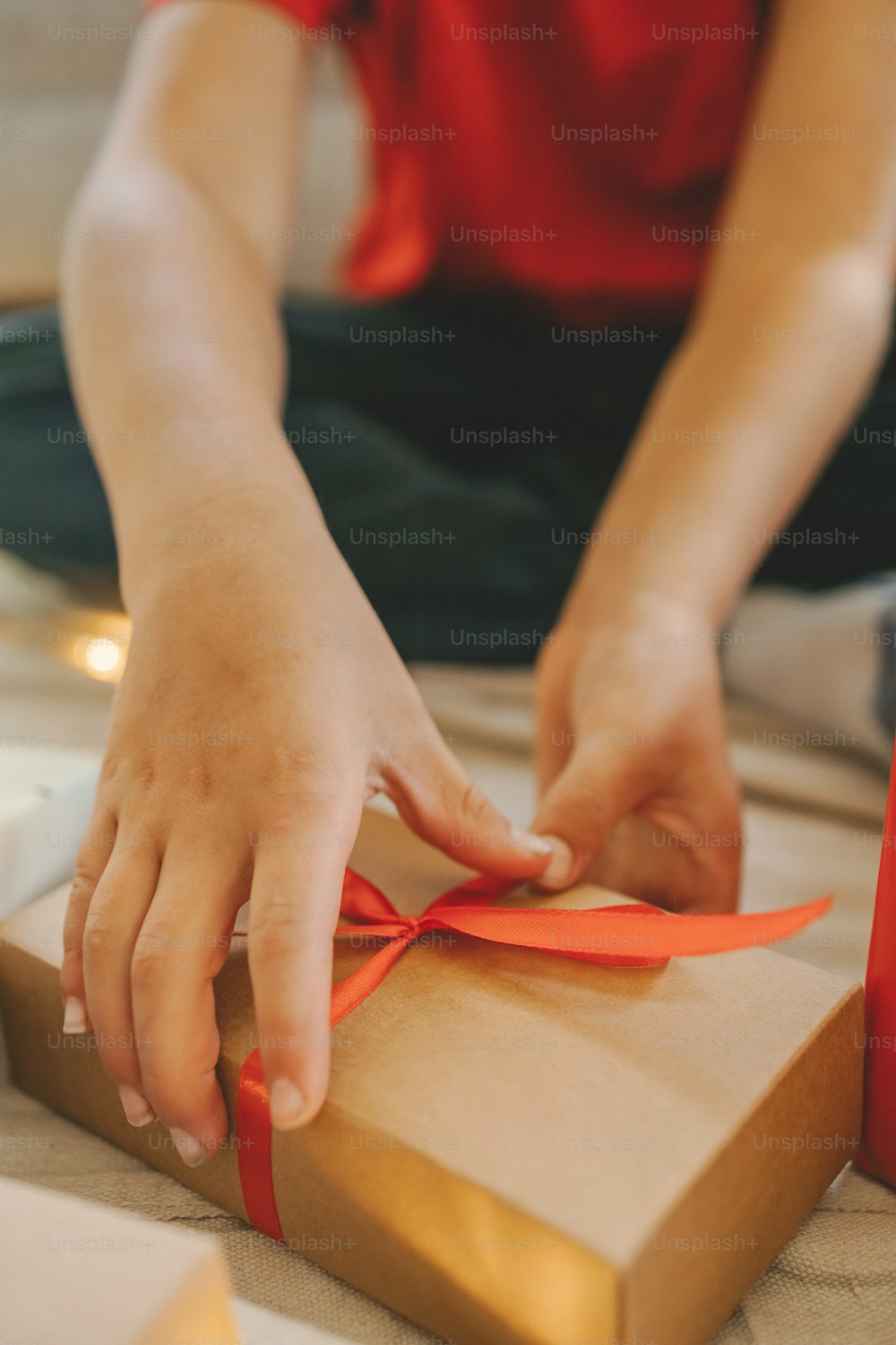 a person tying a red ribbon on a brown box