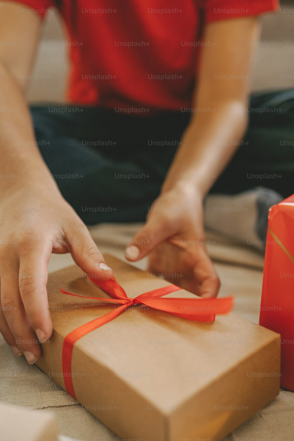 a person opening a brown gift box with a red ribbon