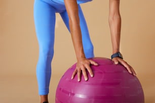 Una mujer con un top azul y leggings está en una pelota de ejercicio rosa
