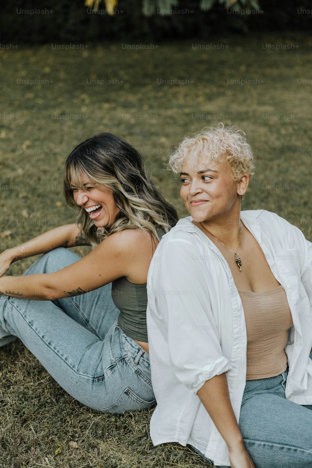 a couple of women sitting on top of a grass covered field