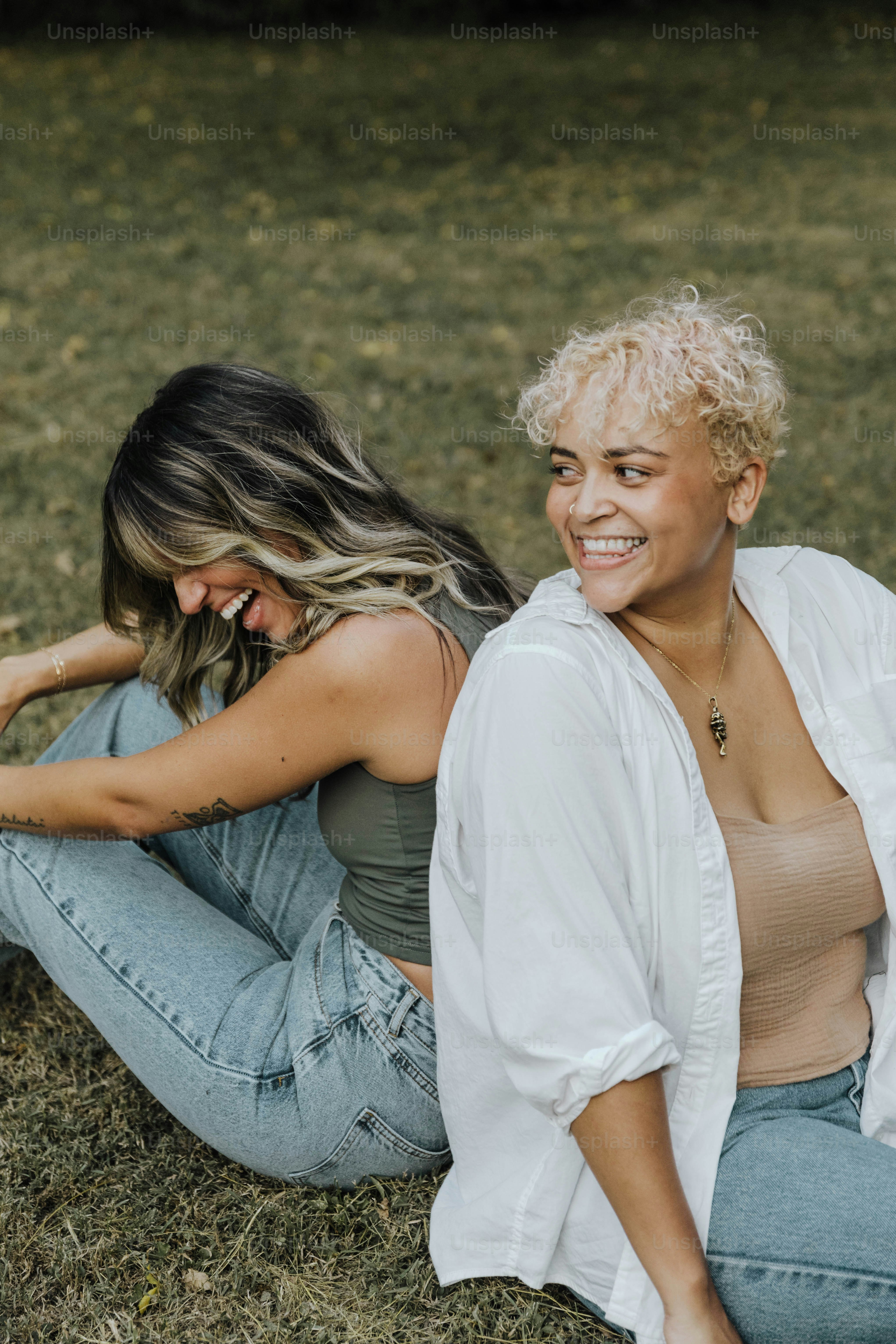 two women are sitting on the grass smiling