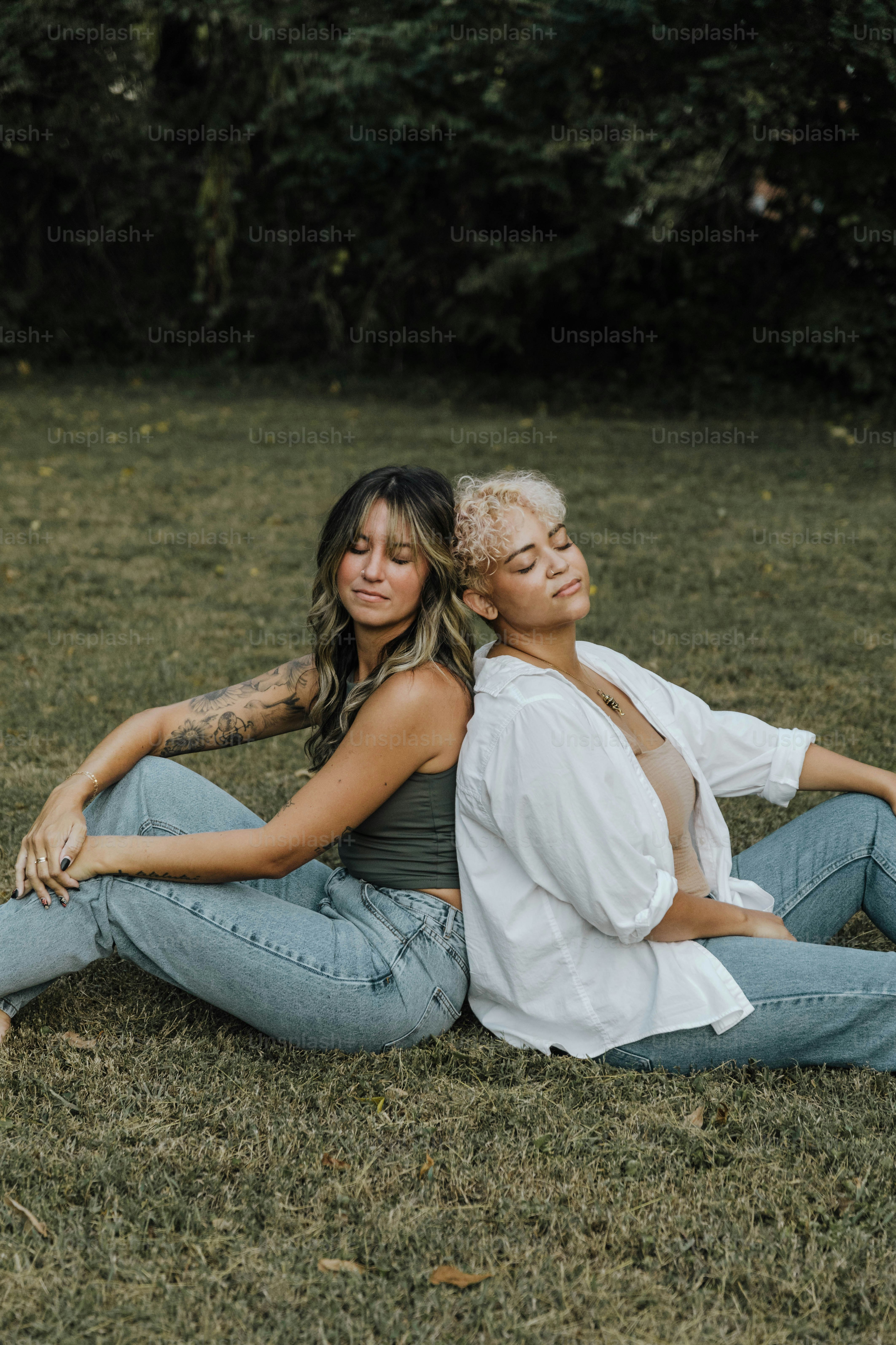 a couple of women sitting on top of a grass covered field